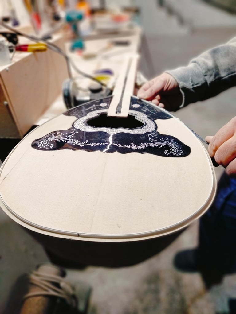 Close-up of hands holding a guitar body with decorative dark blue inlay design during instrument construction or repair