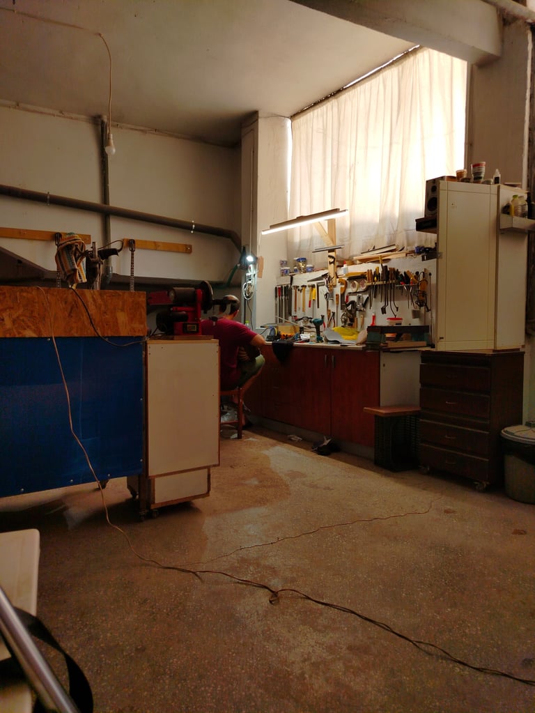 A workshop interior with wooden workbenches, tool storage, and hanging tools against white brick walls with windows