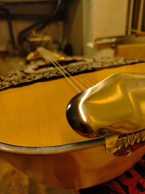 Κοντινό πλάνο σώματος ακουστικής κιθάρας με χορδές και λουρί πάνω σε κόκκινο ύφασμα