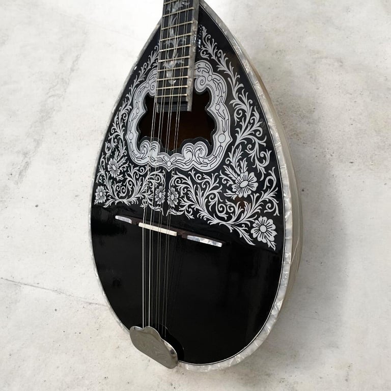 Black and white decorative teardrop-shaped mandolin with ornate floral inlay design on neck and body, displayed against white wall