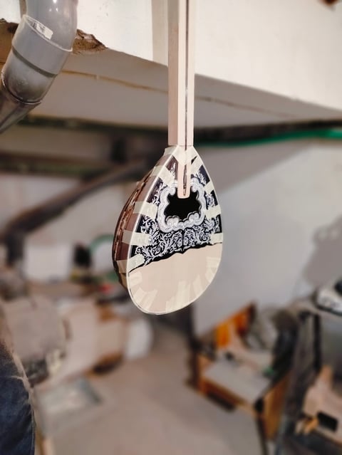 Close-up of a decorative teardrop pendant with black ink design hanging from a white cord in a workshop setting.