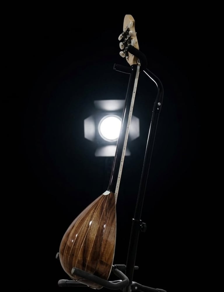 Traditional stringed instrument with wooden round body and long neck on stand with stage lighting in background
