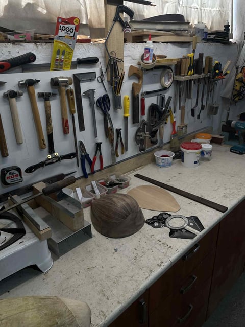 Organized workshop wall with hand tools, hammers, and wrenches displayed above a workbench cluttered with supplies and wooden bowls