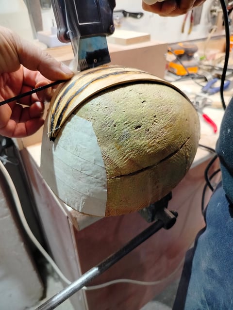 A person holding a spherical stone artifact being scanned with a handheld 3D scanner in a workshop setting