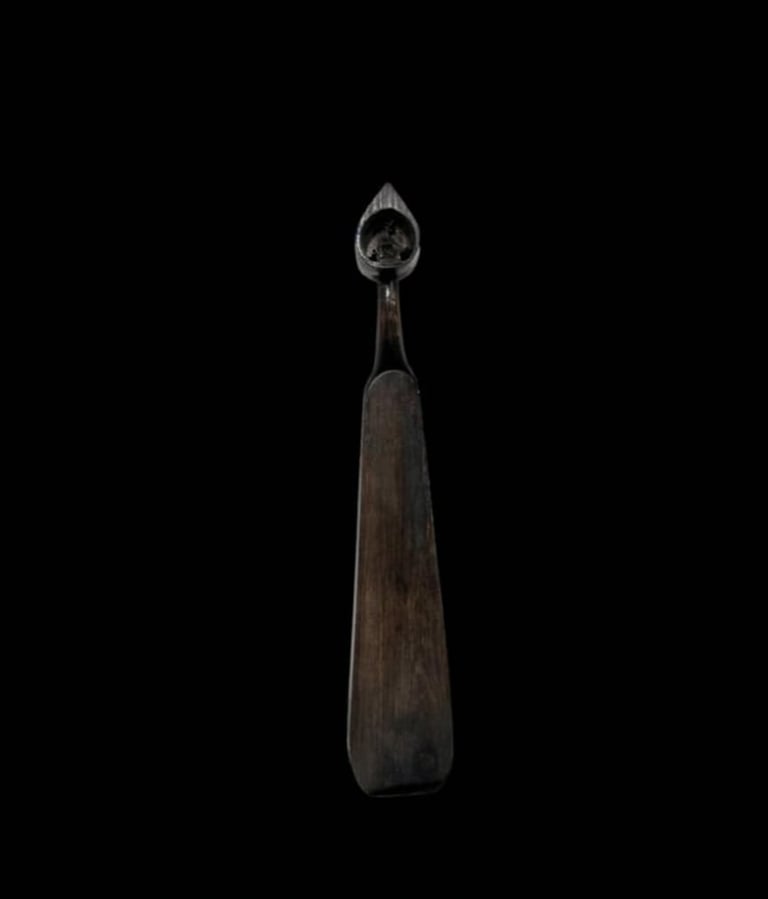 Antique wooden spoon with decorative metal handle featuring ornate teardrop-shaped top against black background
