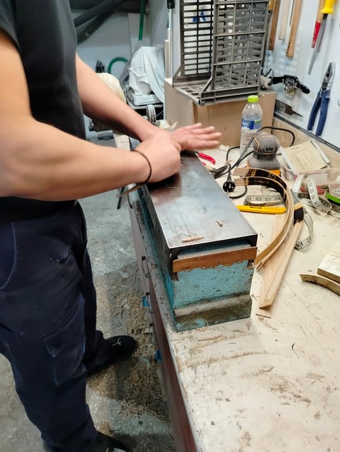 Persons hands working at a cluttered workbench in a workshop, with tools and storage drawers visible in background