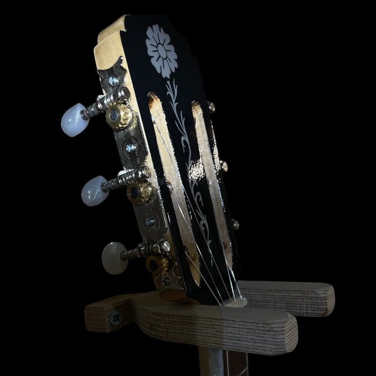 Close-up of guitar headstock with decorative inlays, tuning pegs with blue and clear stones, and wooden base against black background