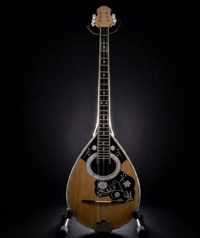 A wooden mandolin with a teardrop-shaped body, ornate pickguard, and dark fretboard against a black background.