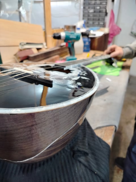 Guitar being repaired in a workshop with tools and materials visible, person working on the instruments body