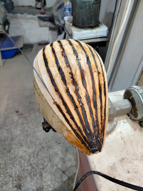Wooden decorative piece with black striped burn marks displayed on a stand in a workshop setting