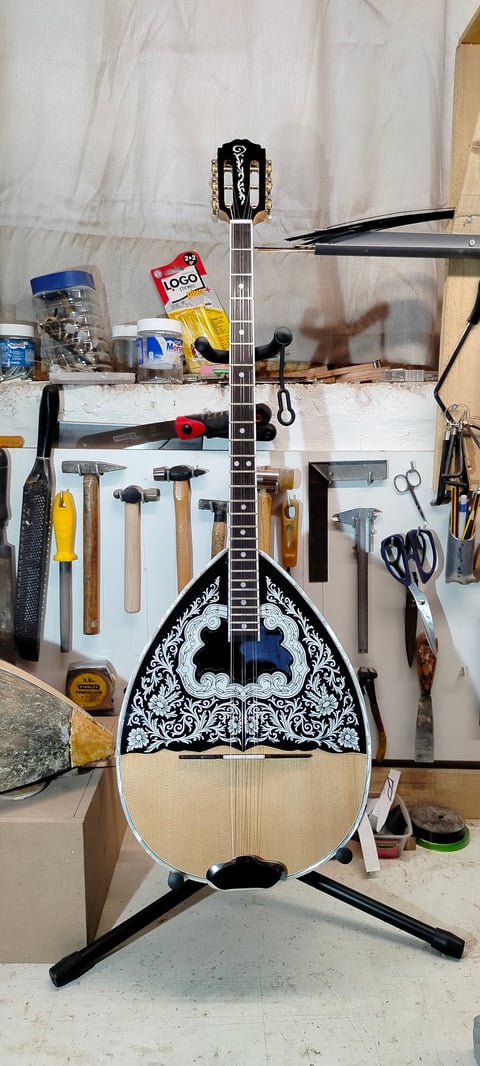 Ornate mandolin with black and white patterned body displayed on stand in workshop surrounded by various tools and equipment