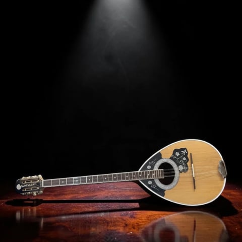 Acoustic mandolin with light wood body and dark fretboard lying on a reflective wooden surface against dark background